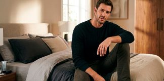 Como Ser um Homem Bom de Cama: O Guia Definitivo para Surpreender Homem confiante sentado na beira da cama em um quarto com iluminação aconchegante, representando o conceito de bom de cama.