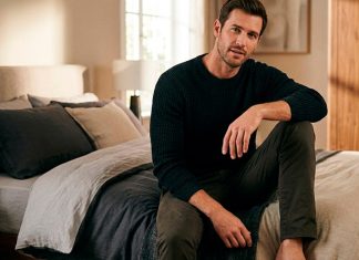 Como Ser um Homem Bom de Cama: O Guia Definitivo para Surpreender Homem confiante sentado na beira da cama em um quarto com iluminação aconchegante, representando o conceito de bom de cama.