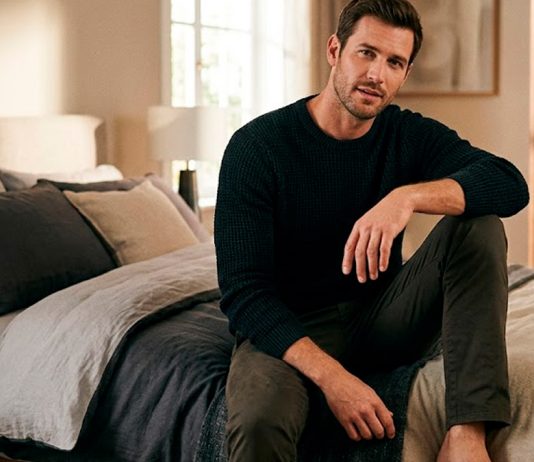 Como Ser um Homem Bom de Cama: O Guia Definitivo para Surpreender Homem confiante sentado na beira da cama em um quarto com iluminação aconchegante, representando o conceito de bom de cama.